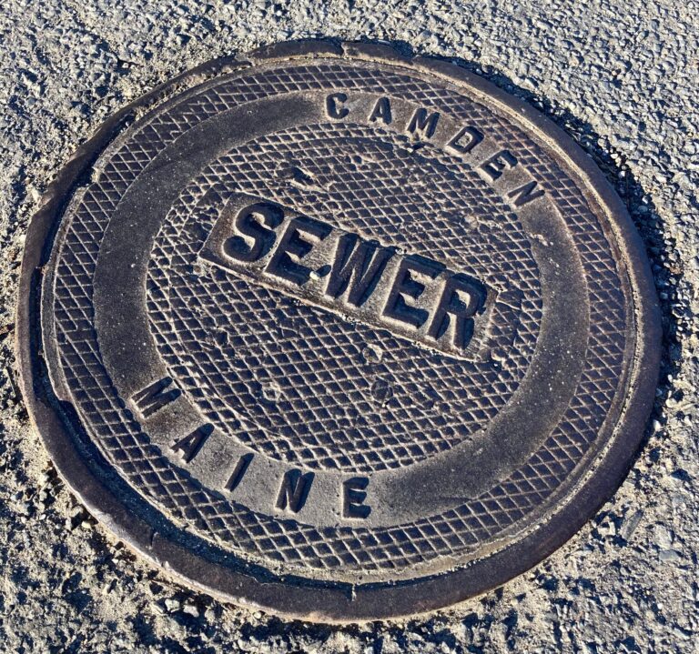 A photograph of a Camden sewer drain that reads "Camden | Maine | Sewer"