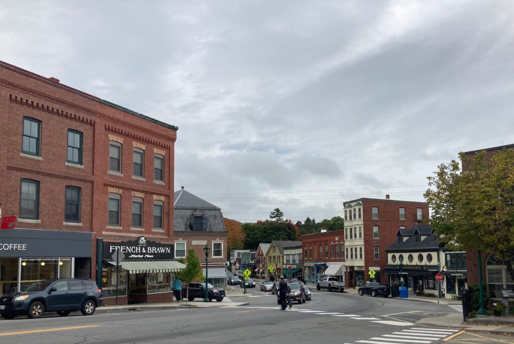 A photograph of a busy street in Camden. Brick and cream colored buildings line the street while cars and motorbikes drive down the street. The weather is overcast, creating a gray cast on the town.